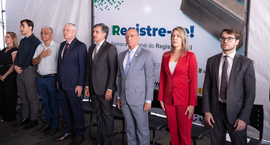 Fotografia de um grupo de oito autoridades perfiladas em pé durante uma cerimônia sob uma tenda ...