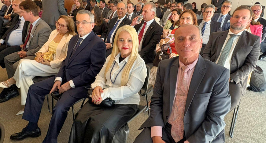 A foto mostra um auditório ou sala de reuniões com várias pessoas sentadas em fileiras, vestindo...