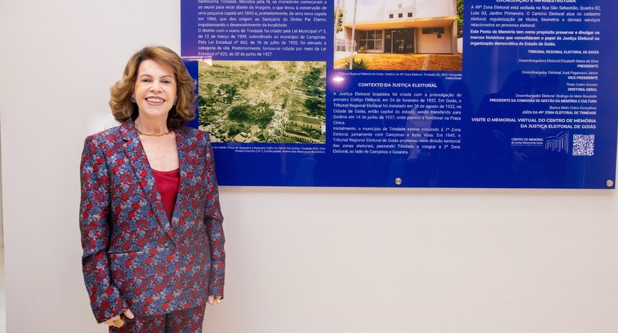 mostra uma mulher branca de pé, à esquerda da imagem, com cabelos castanhos na altura dos ombros...