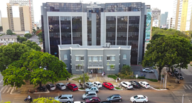 A imagem mostra a fachada de um prédio institucional com estrutura moderna de vidro escuro e col...