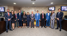 Uma fotografia colorida de plano geral mostra um grupo de doze pessoas, composto por oito homens...