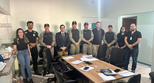 Fotografia em plano médio de nove profissionais reunidos em uma sala de reuniões, posicionados l...