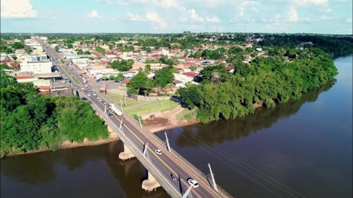 Vista aérea de uma pequena cidade atravessada por um rio largo. Uma ponte de concreto liga as du...