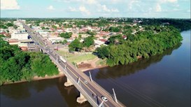 Vista aérea de uma pequena cidade atravessada por um rio largo. Uma ponte de concreto liga as du...