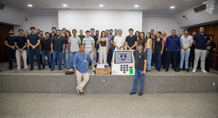 A imagem mostra um grande grupo de pessoas sorridentes posando para uma fotografia em cima de um...