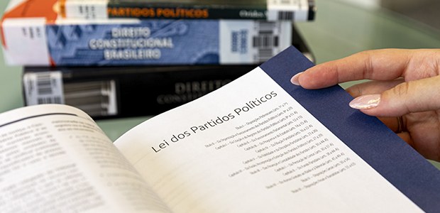 Foto: Alejandro Zambrana/Secom/TSE - Lei dos partidos políticos - 19.09.2025 A imagem mostra uma mão feminina folheando um livro aberto. A página visível apresenta o título ...