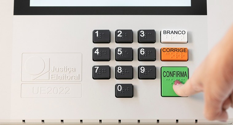 Foto mostra dedo indicador de uma mulher apertando a tecla verde "Confirma" na urna eletrônica
