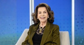 A imagem apresenta uma senhora sorridente a olhar diretamente para a câmara num ambiente que par...