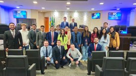Fotografia em grupo de cerca de vinte pessoas posando sorridentes em um auditório ou plenário, a...