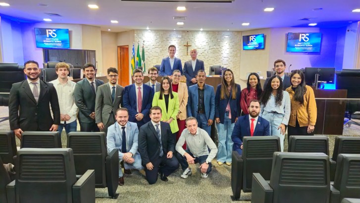 Fotografia em grupo de cerca de vinte pessoas posando sorridentes em um auditório ou plenário, a...