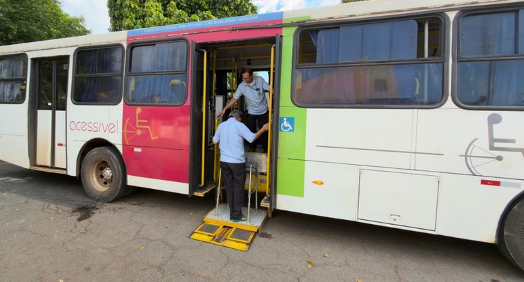 Um ônibus branco está parado em uma rua asfaltada, mostrando sua porta lateral aberta com um ele...