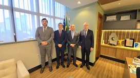 Quatro homens de terno estão em pé lado a lado em um escritório institucional, posando para uma ...