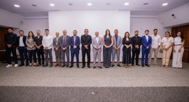 Uma fotografia em plano médio e horizontal captura um grupo de 18 pessoas perfiladas lado a lado...