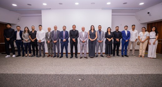 Uma fotografia em plano médio e horizontal captura um grupo de 18 pessoas perfiladas lado a lado...