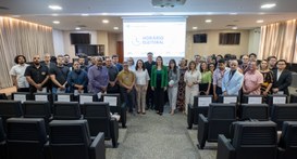mostra um grande grupo de pessoas reunidas para um evento oficial, em pé diante de um telão que ...