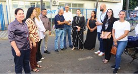 Um grupo diversificado de cerca de onze pessoas está reunido ao ar livre em frente a um prédio c...