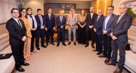 Uma fotografia em plano médio mostra um grupo de doze pessoas, sendo três mulheres e nove homens...