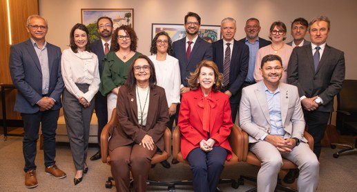 A fotografia registra um grupo de treze pessoas reunidas em um ambiente formal e acolhedor de es...