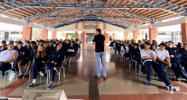 Eleitores do Futuro educação cidadã no Colégio Estadual Senador Onofre Quinan Foto em plano geral de uma palestra em um pátio escolar coberto. Em primeiro plano, um homem de ...