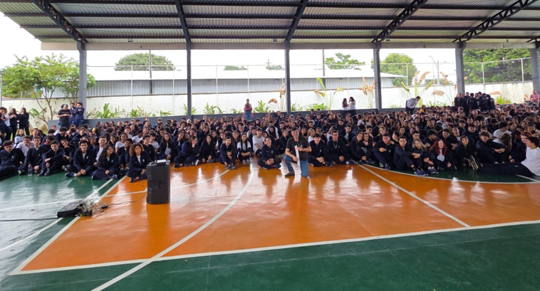 Eleitores do Futuro leva atendimentos e palestra educativa ao Colégio Estadual Jardim Vila Boa Fotografia de uma grande plateia de jovens estudantes, a maioria vestindo uniformes azul-escuros...