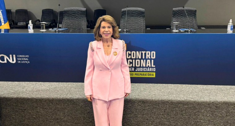 Uma mulher de pele clara e cabelos castanhos volumosos na altura dos ombros sorri para a câmera,...