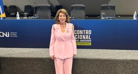 Uma mulher de pele clara e cabelos castanhos volumosos na altura dos ombros sorri para a câmera,...