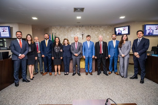 Uma fotografia colorida de plano geral mostra um grupo de doze pessoas, composto por oito homens...