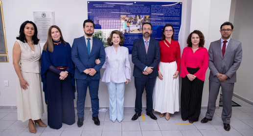 Uma fotografia interna em plano inteiro mostra um grupo de oito pessoas, cinco mulheres e três h...